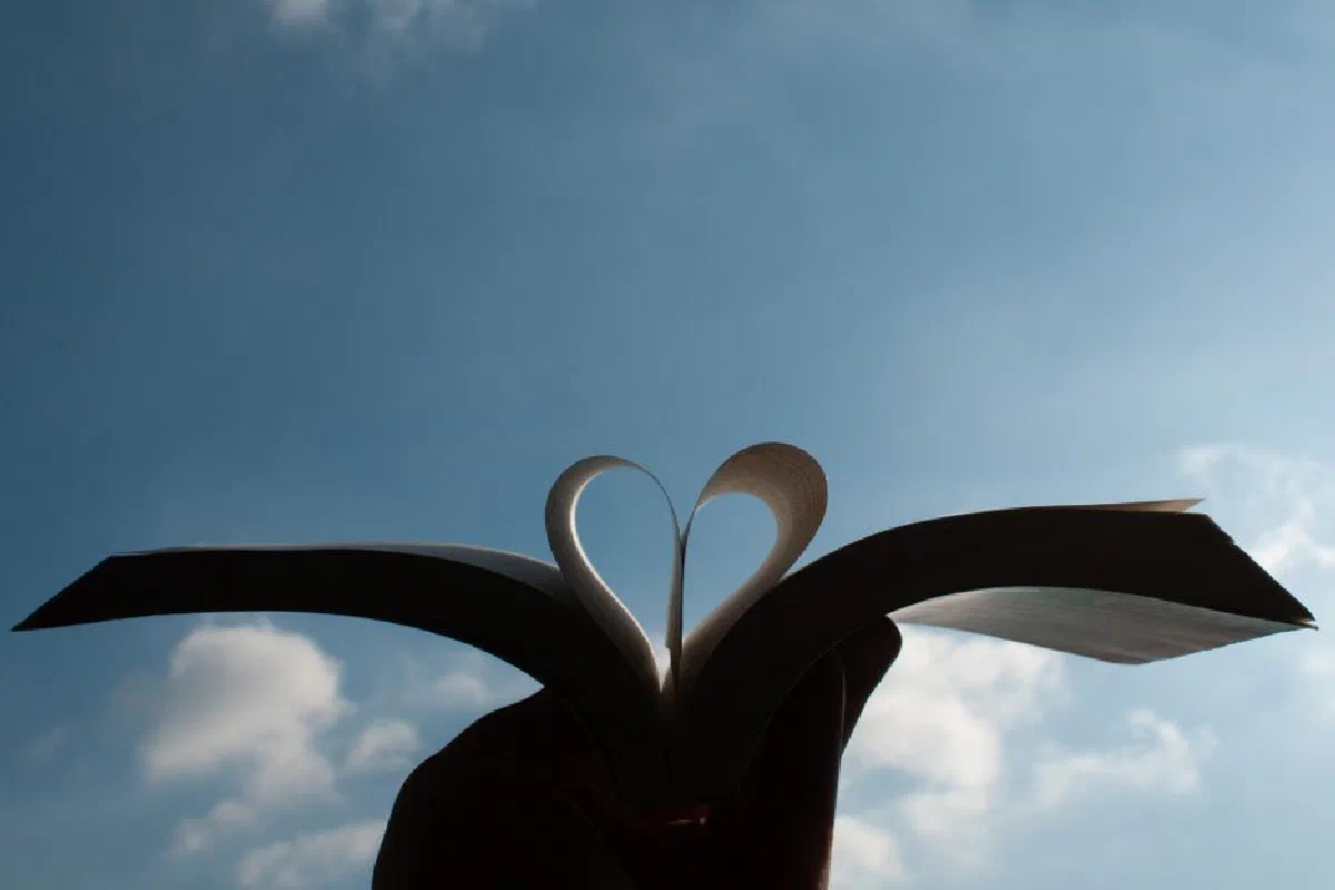 A heart shape formed by an open book's pages with a clear blue sky background in Milano, Italy.
