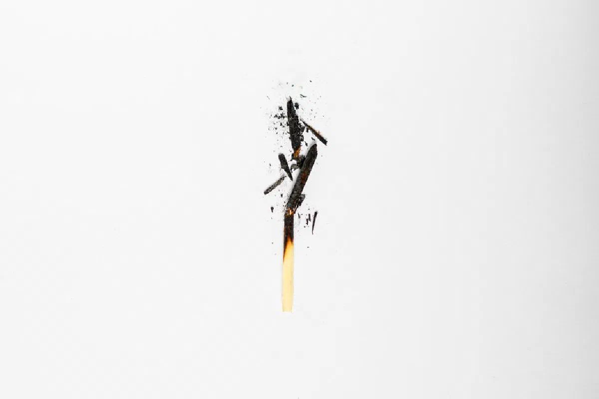Minimalist image of a burnt matchstick with scattered ash on white background.