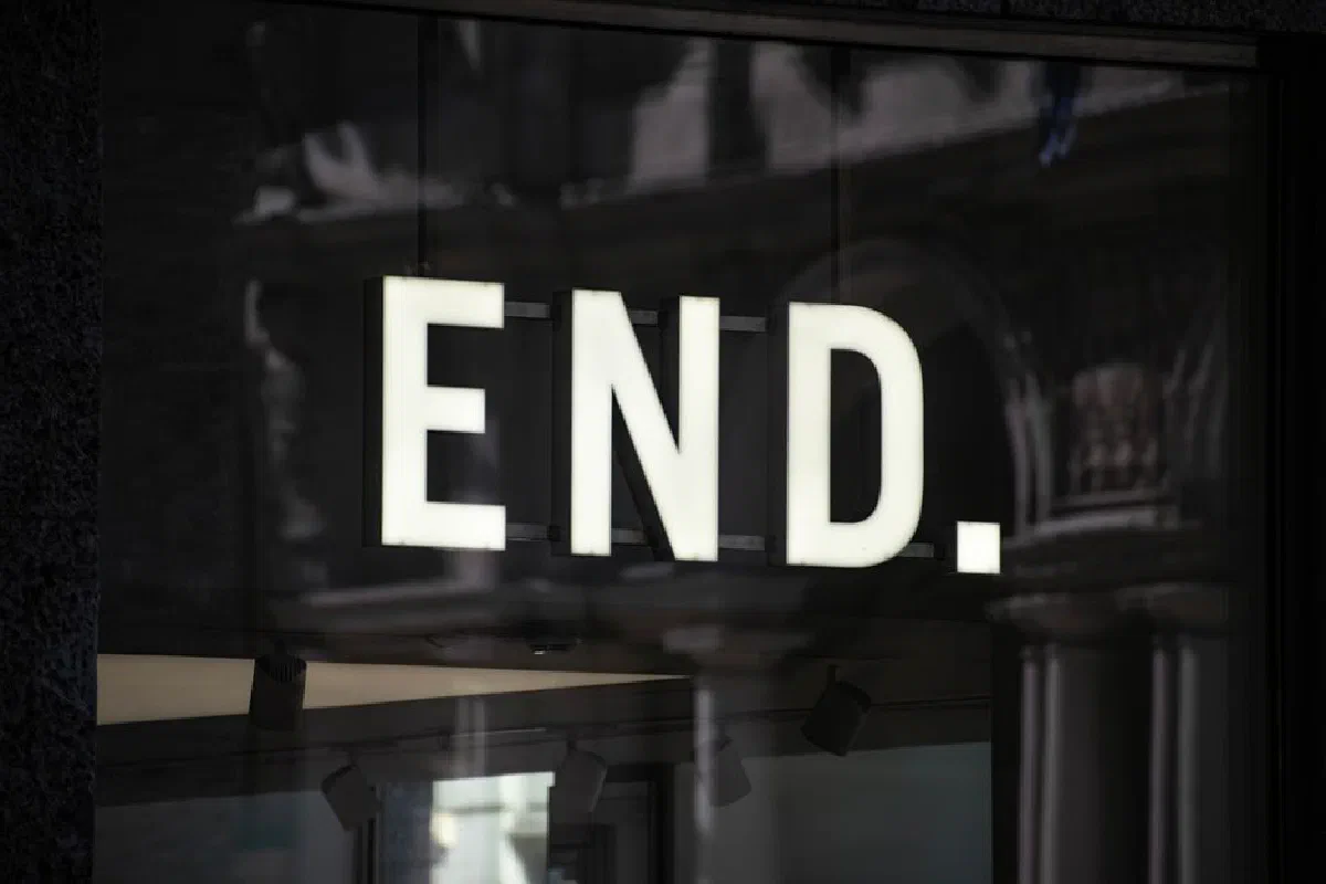 A glowing 'End' sign displayed in a shop window in Milan, reflecting urban architecture.