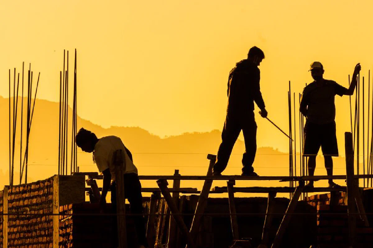 Silhouetted workers on a construction site at sunset, highlighting the manual labor involved.