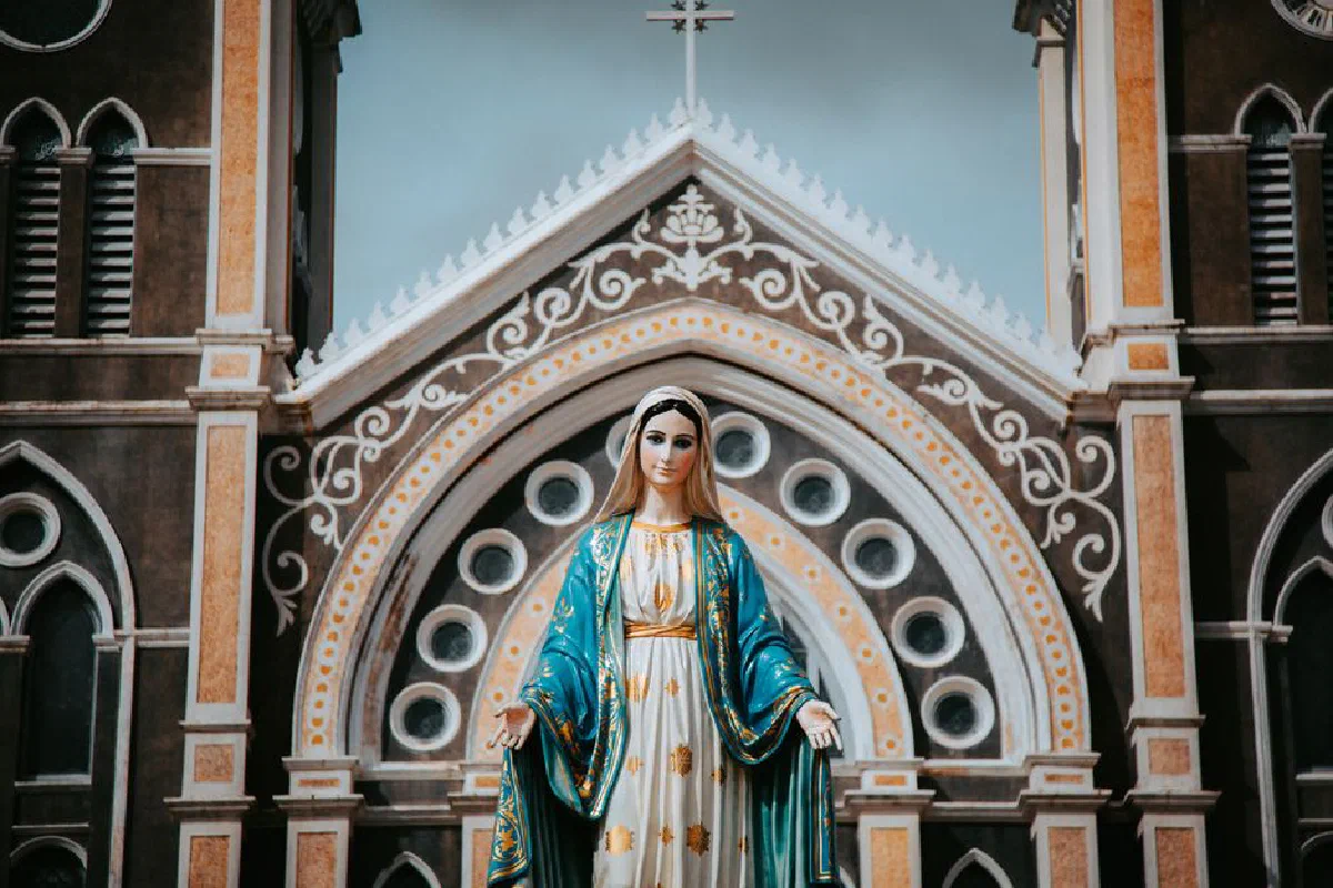 Vibrant statue of the Virgin Mary in front of an ornate church facade.