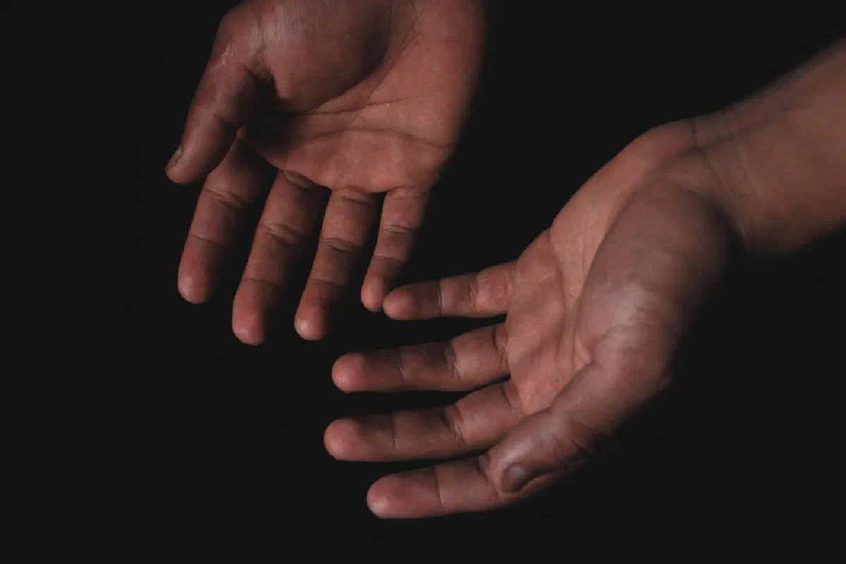 Close-up image of two hands with palms open against a black background, highlighting human skin texture.