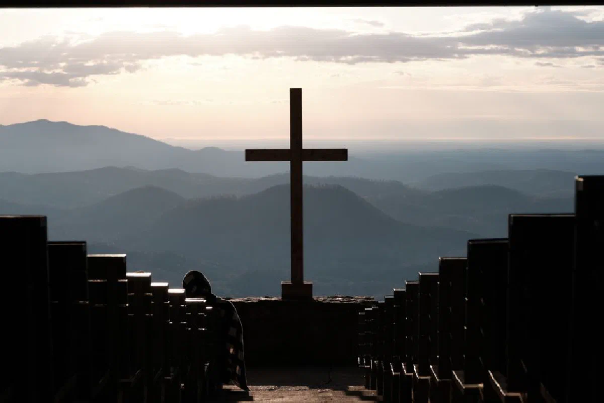 A tranquil sunrise over mountains with a cross in the foreground, symbolizing peace and spirituality.
