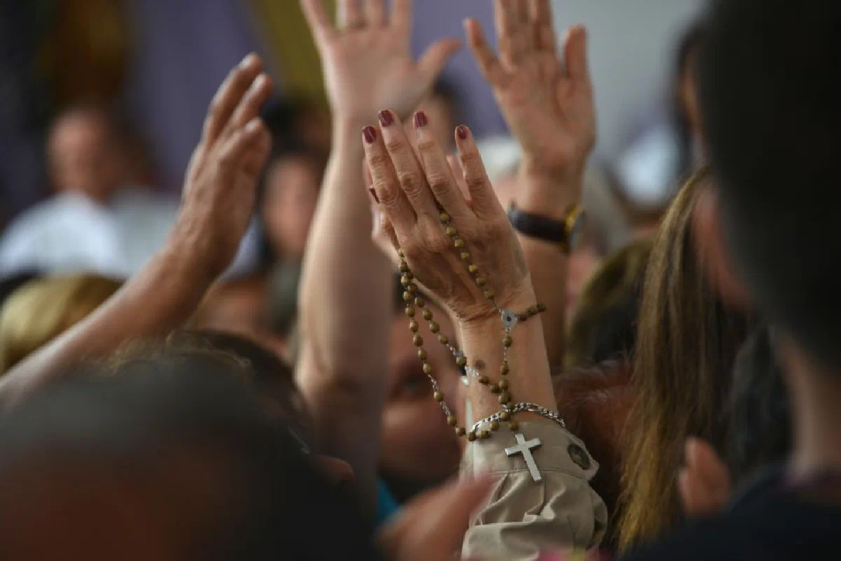 A crowd of people raising hands in a religious gathering, holding a rosary.