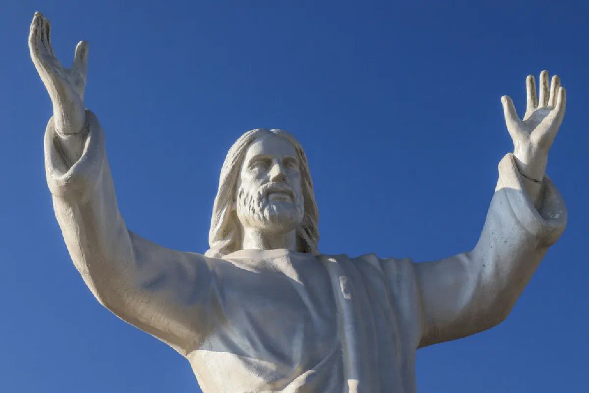 Majestic statue of Jesus with arms raised under a clear blue sky, symbolizing peace and hope.