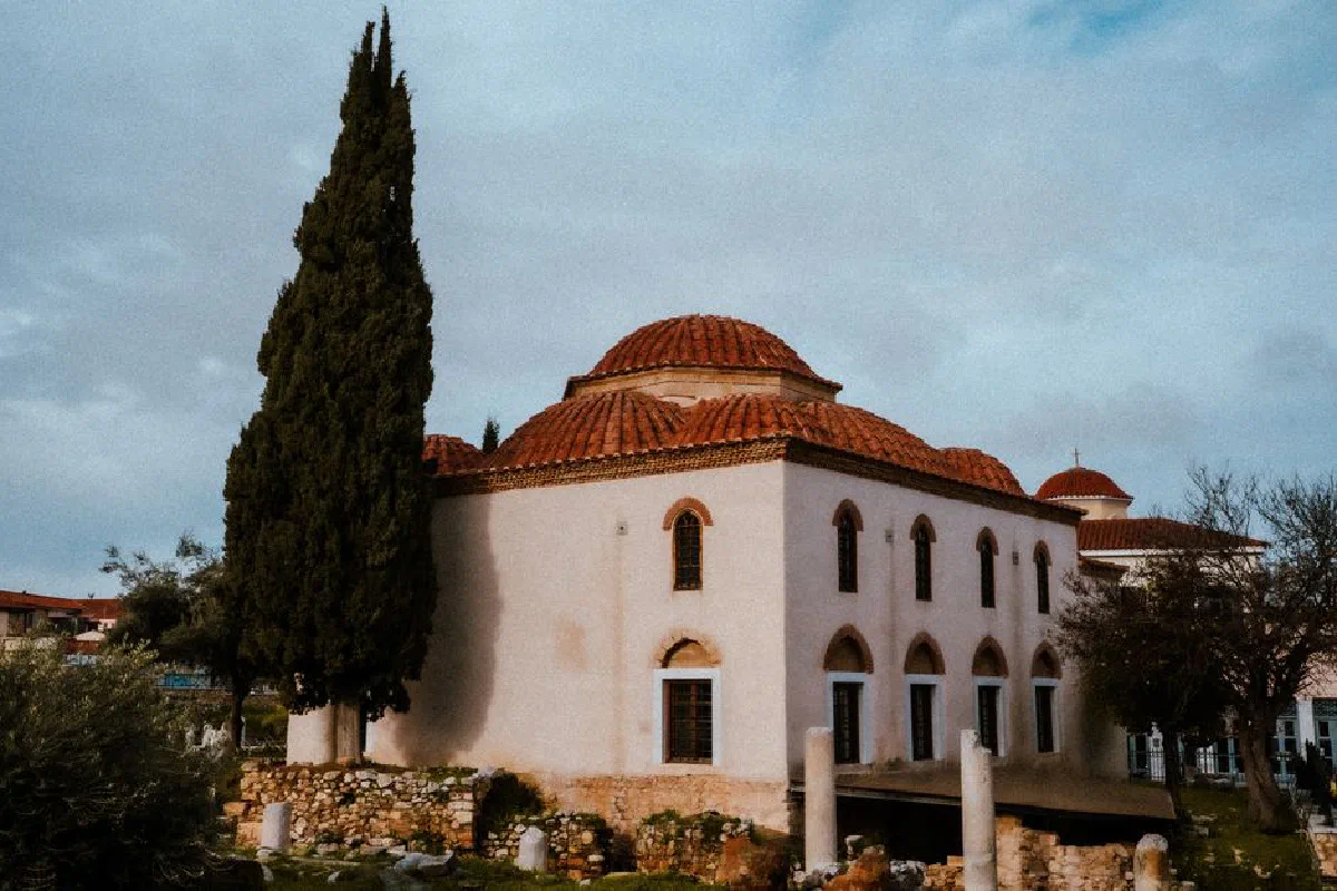 Beautiful historic church building with red dome roof beside a tall cypress tree under a cloudy sky.