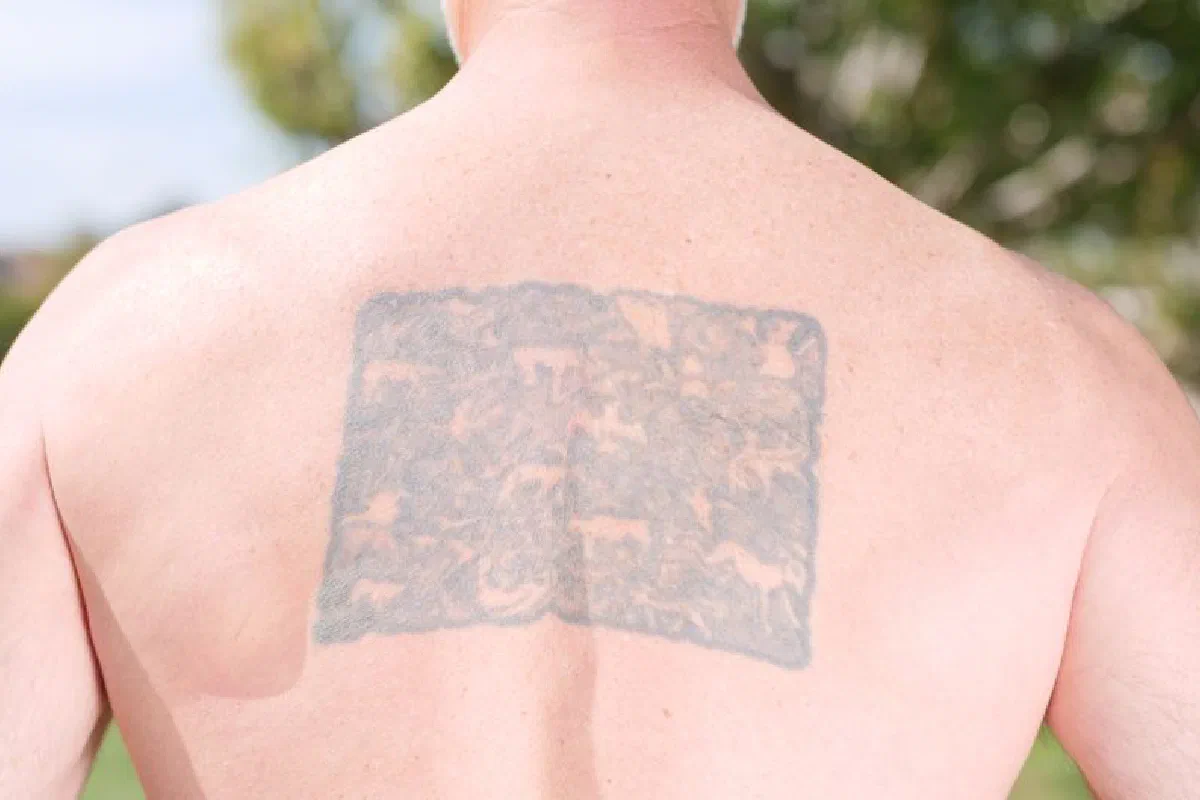 Close-up of a man's back with a tattoo in an outdoor setting.