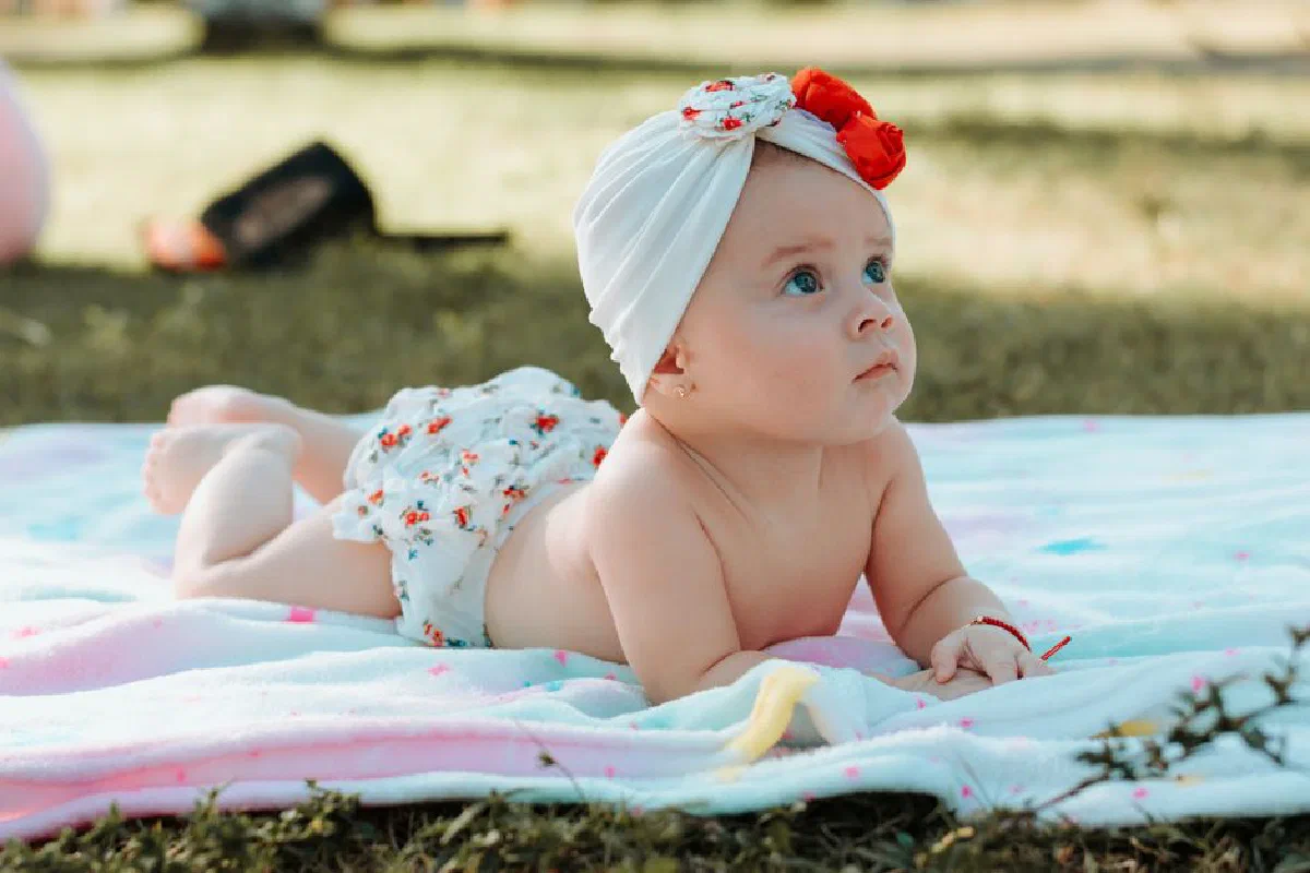 Cute baby lying on a blanket outdoors during the day, wearing a white headband.