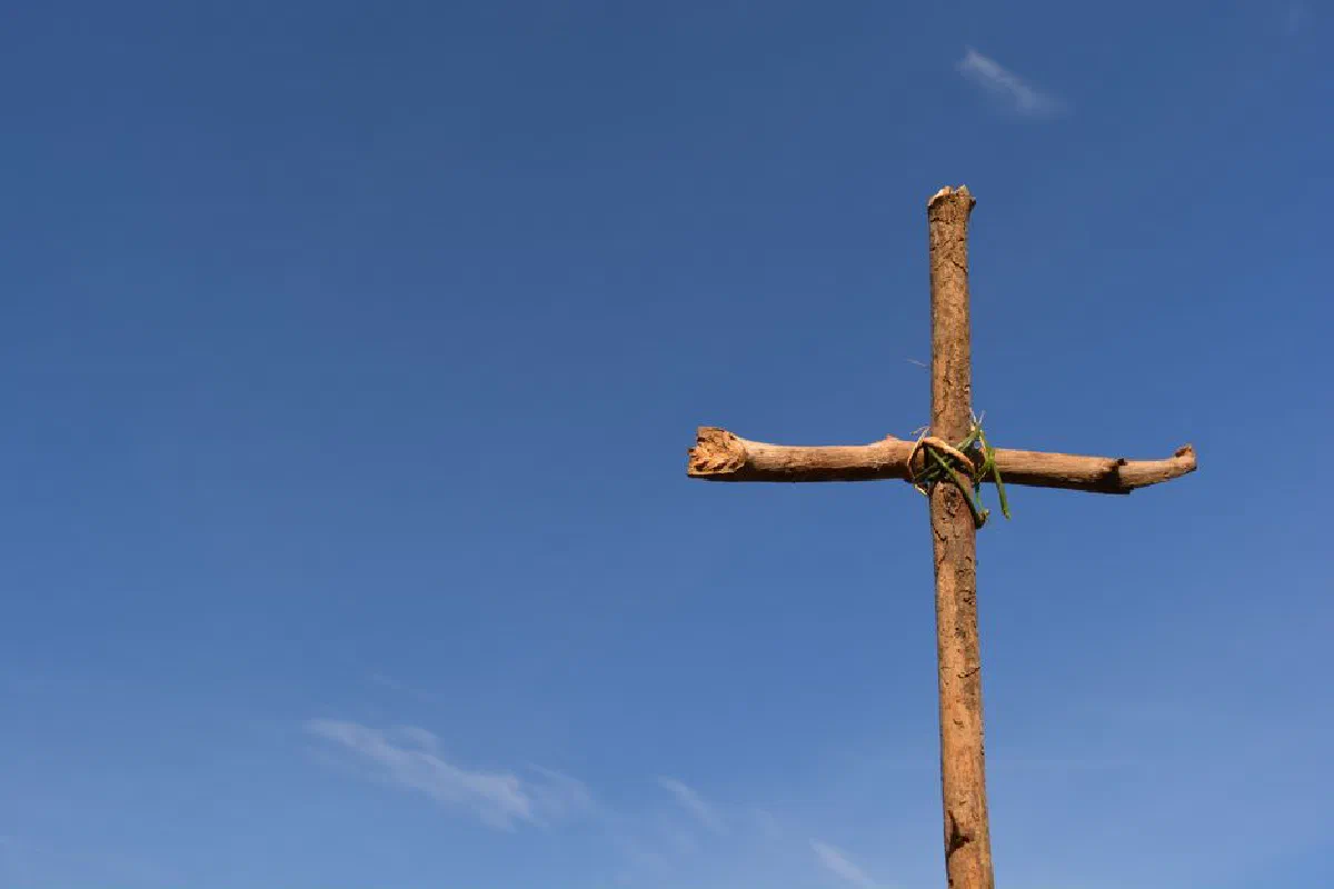 A rustic wooden cross stands against a clear blue sky, symbolizing faith and spirituality.