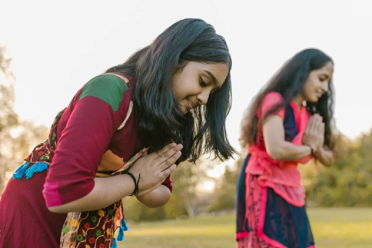 Two women practicing yoga with namaste pose outdoors in the field.
