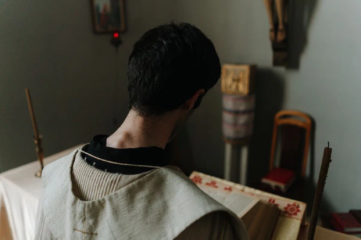 A priest reads a book in a solemn church setting, emphasizing religious devotion.