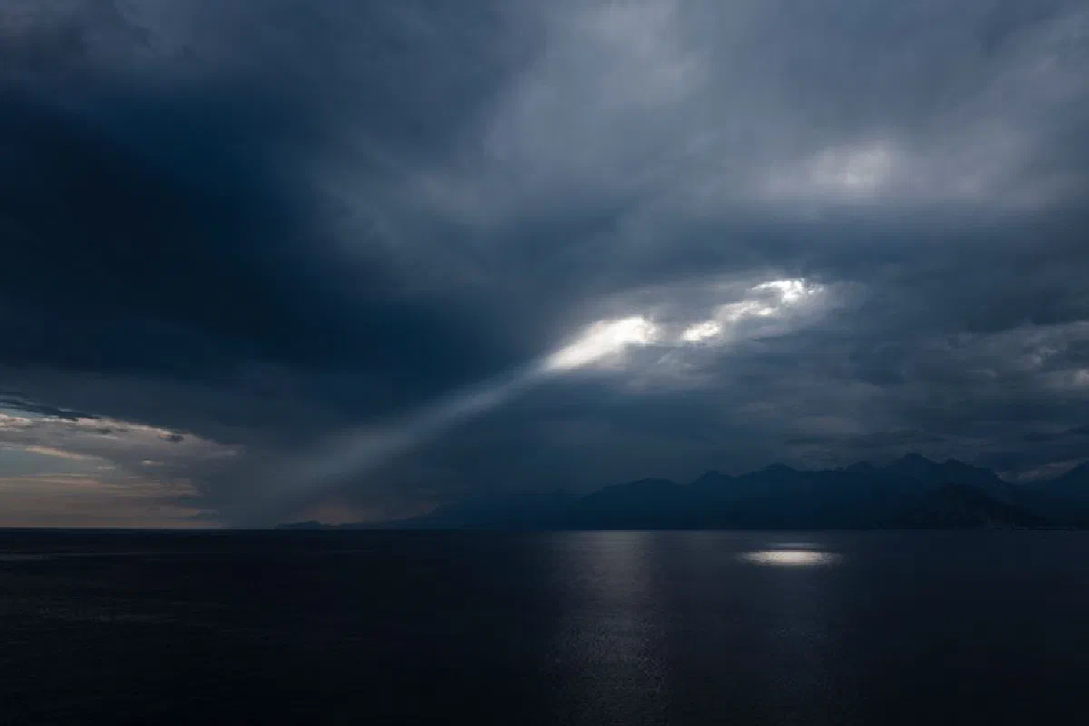An atmospheric coastal view with sunrays piercing dramatic clouds over the ocean.
