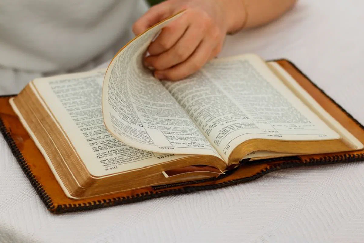 A person's hand turning pages of an open Bible, creating a peaceful study scene.