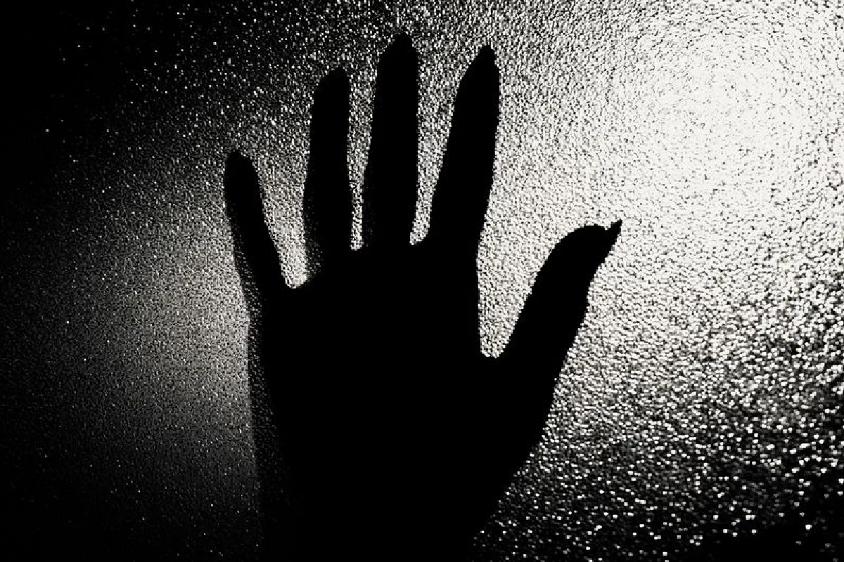 A dramatic silhouette of a hand pressed against a textured glass surface, creating a mysterious atmosphere.