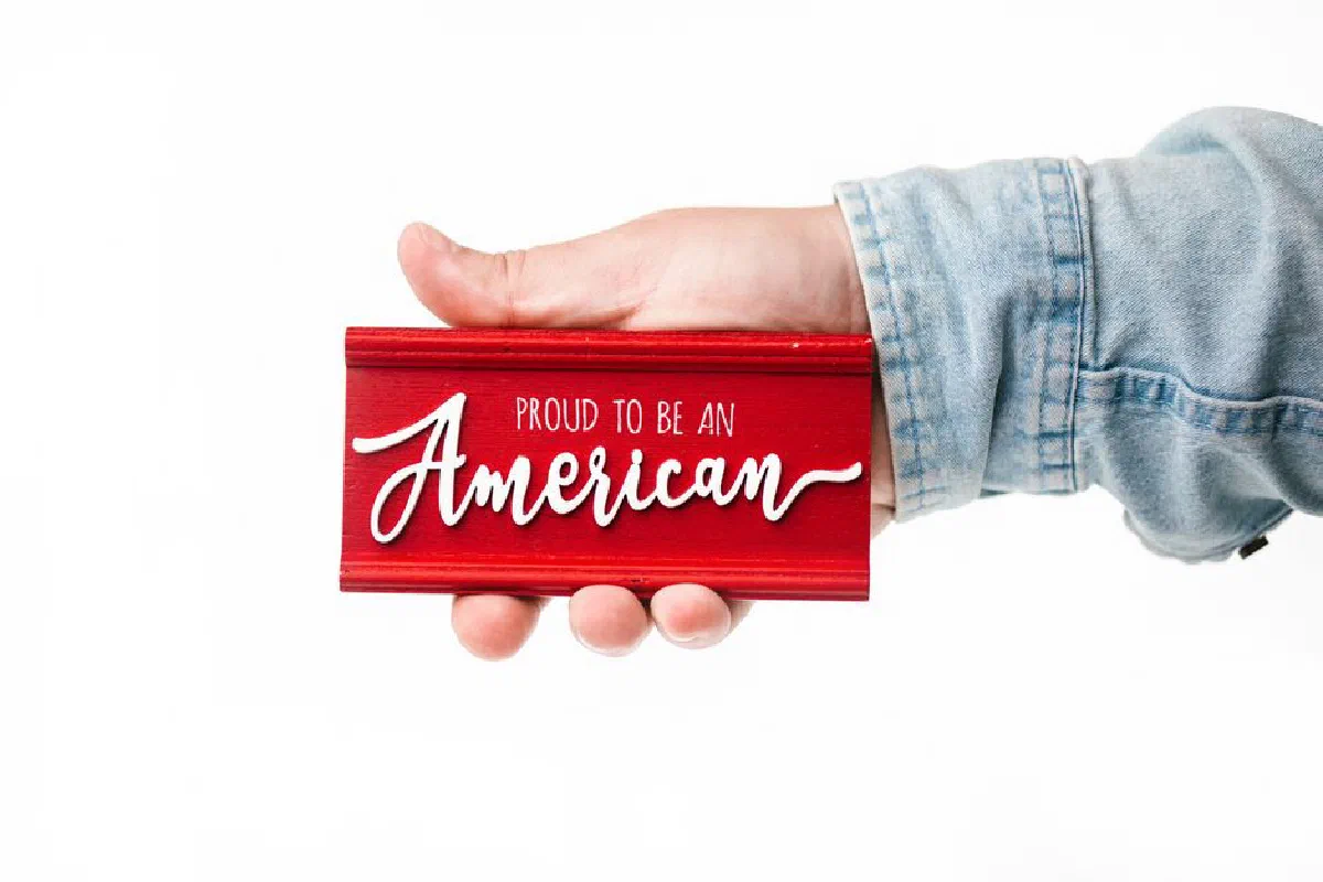 Hand holding a red sign with 'Proud to be an American' text, celebrating patriotism.