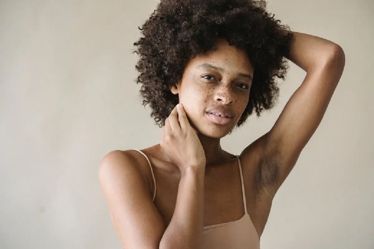 Close-up of a woman with afro hair and freckles posing thoughtfully in a studio setting.