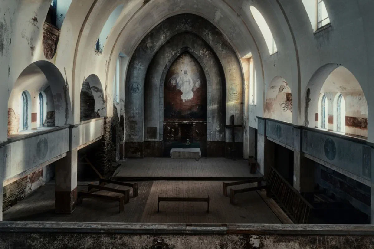 A view of a weathered and abandoned church interior with arched ceilings and wooden pews.