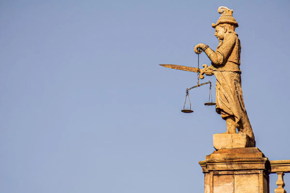 A side view of a justice statue with a sword and weighing scales against blue skies.
