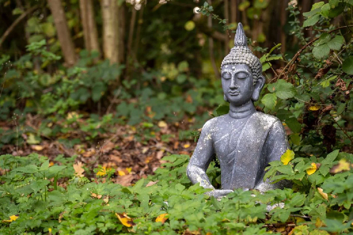 Buddha statue surrounded by lush green leaves in a tranquil garden, promoting spirituality and calm.
