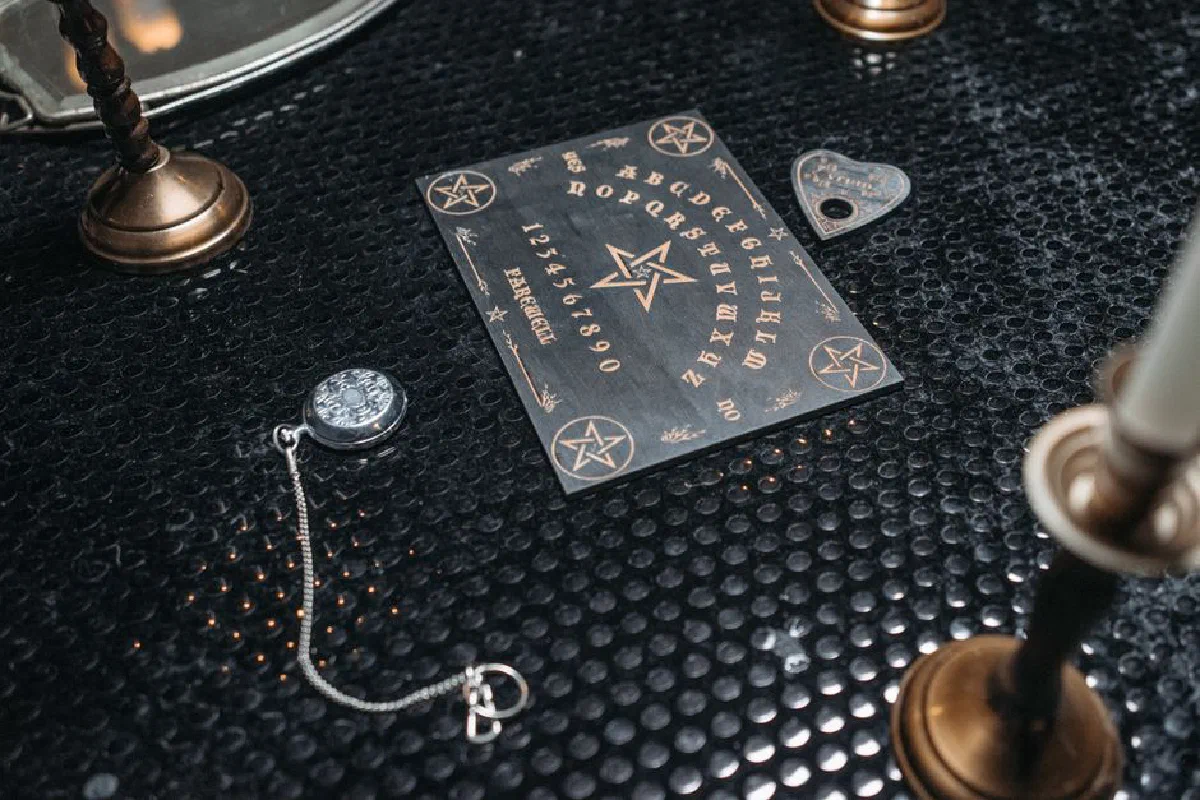 A mystical Ouija board setup on a textured black table, surrounded by candles and spiritual items.