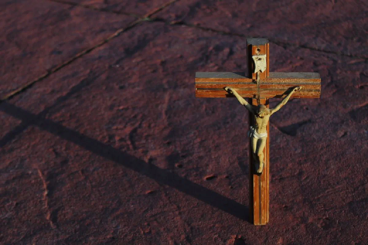 A wooden crucifix casting a shadow on a textured red stone surface.