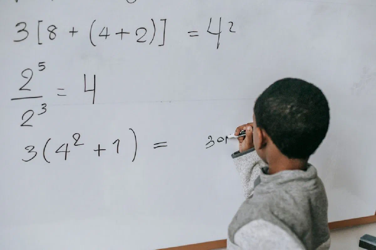 Back view of anonymous African American boy writing on whiteboard while doing sums on mathematics class