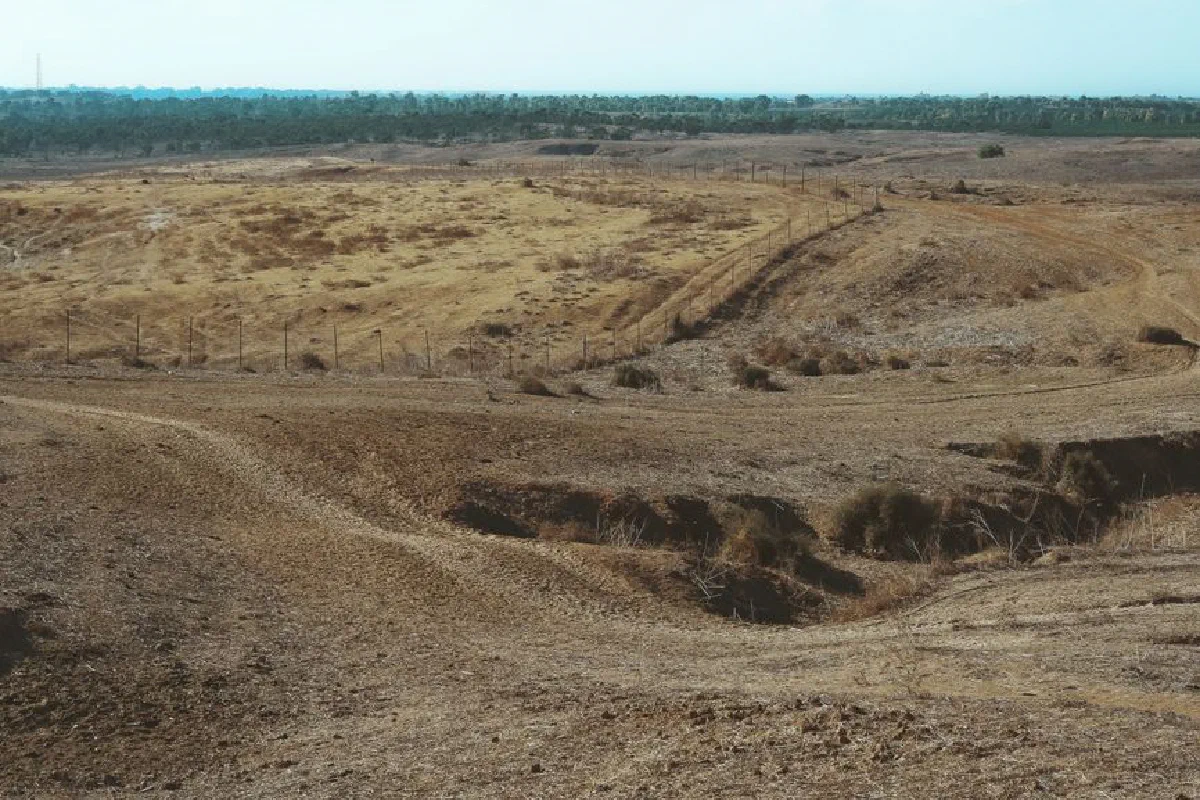 A vast, dry landscape depicting arid soil and sparse vegetation under a clear sky.
