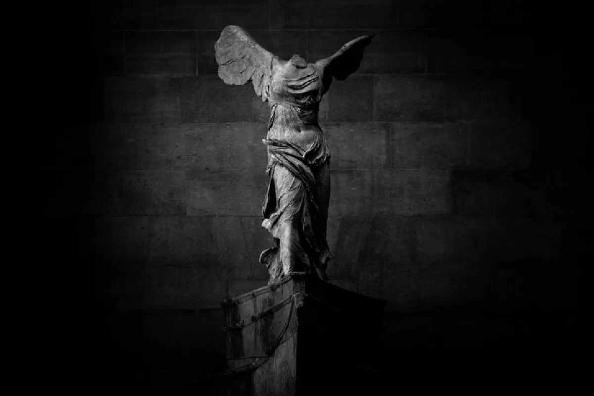 Iconic Winged Victory of Samothrace statue at the Louvre, Paris, in a dramatic black and white setting.