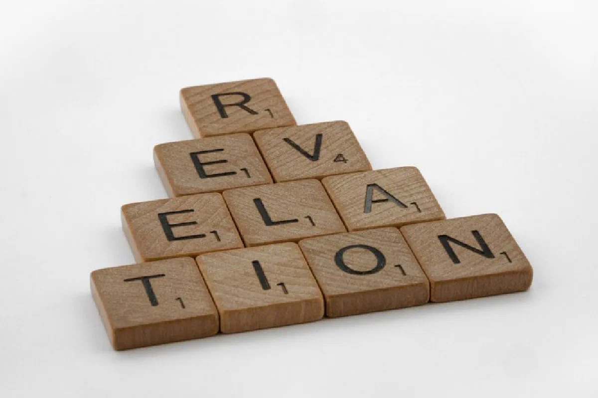 Wooden Scrabble tiles arranged to spell 'Revelation' on a white background, ideal for educational themes.