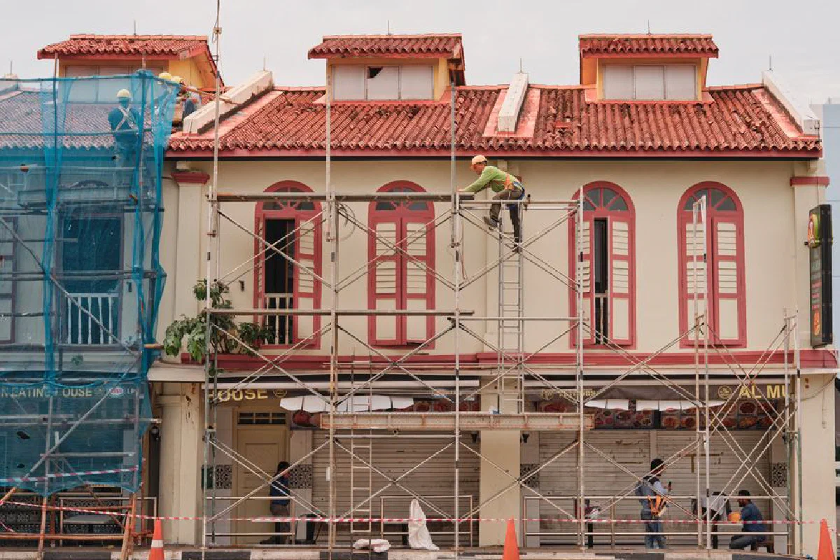 Workers on scaffolding renovating a historic building facade with red roof and tall windows.