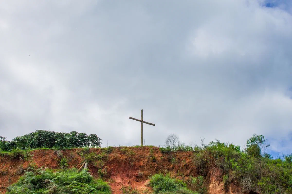 A serene hilltop view with a wooden cross under a cloudy sky in Castelo, Espírito Santo, Brazil.