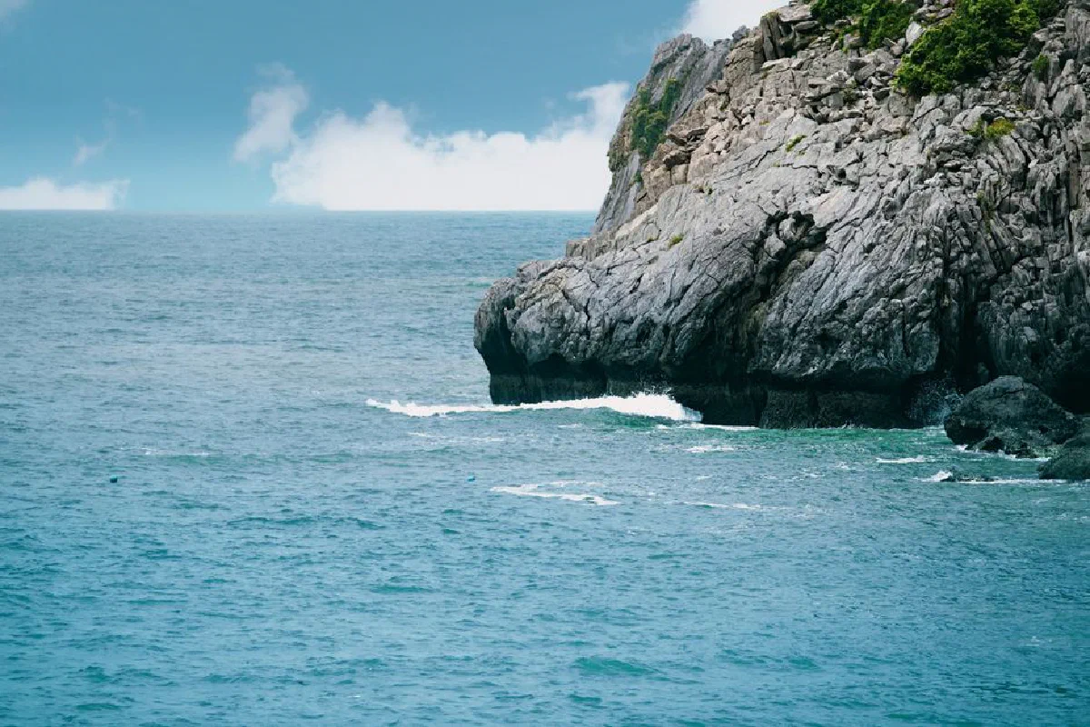 A striking rocky sea cliff with blue ocean waves and cloud-dappled sky.