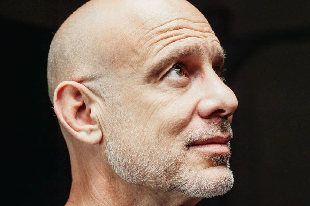 Close-up profile of a senior bald bearded man looking upwards against a dark background.
