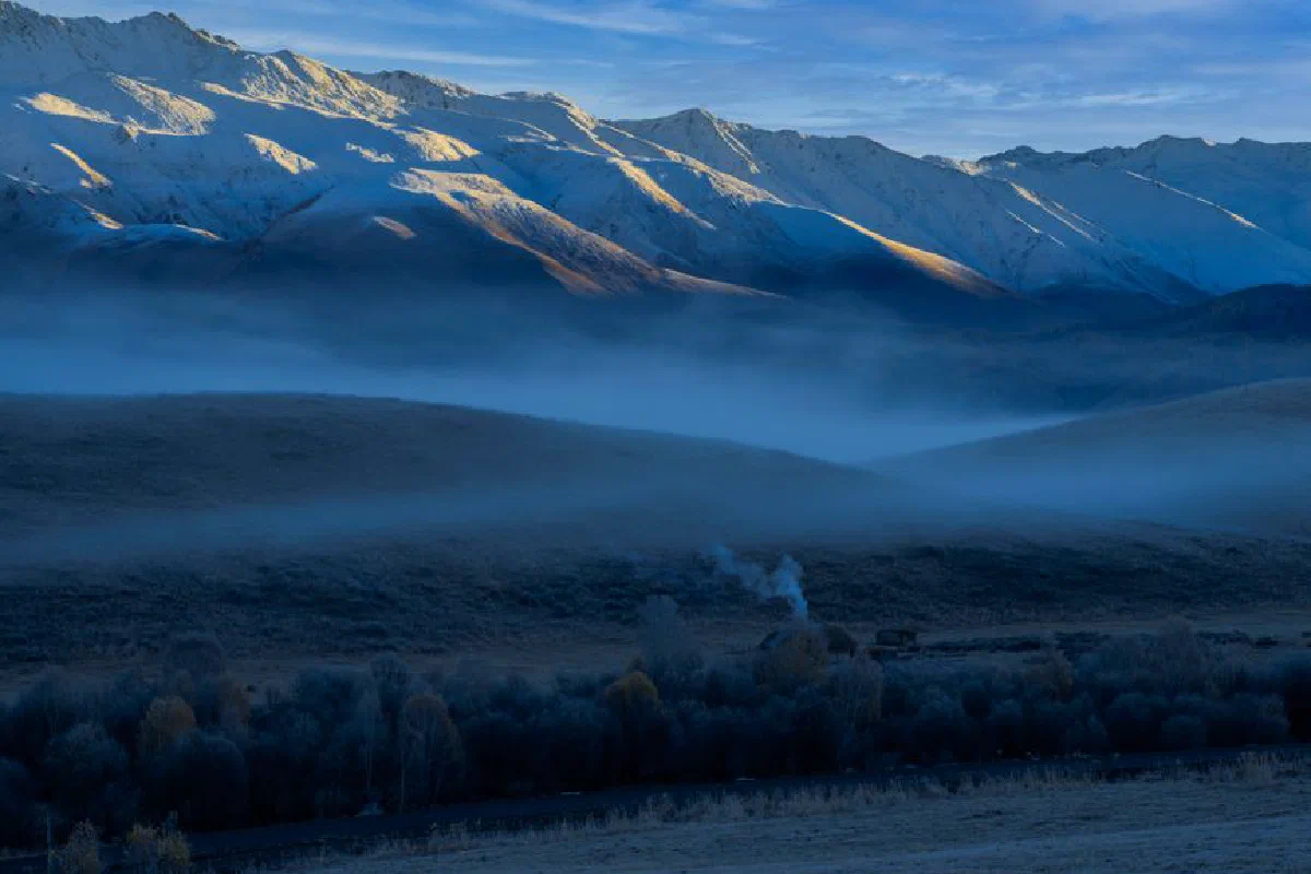 Breathtaking view of snow-covered mountains with misty fields at twilight.