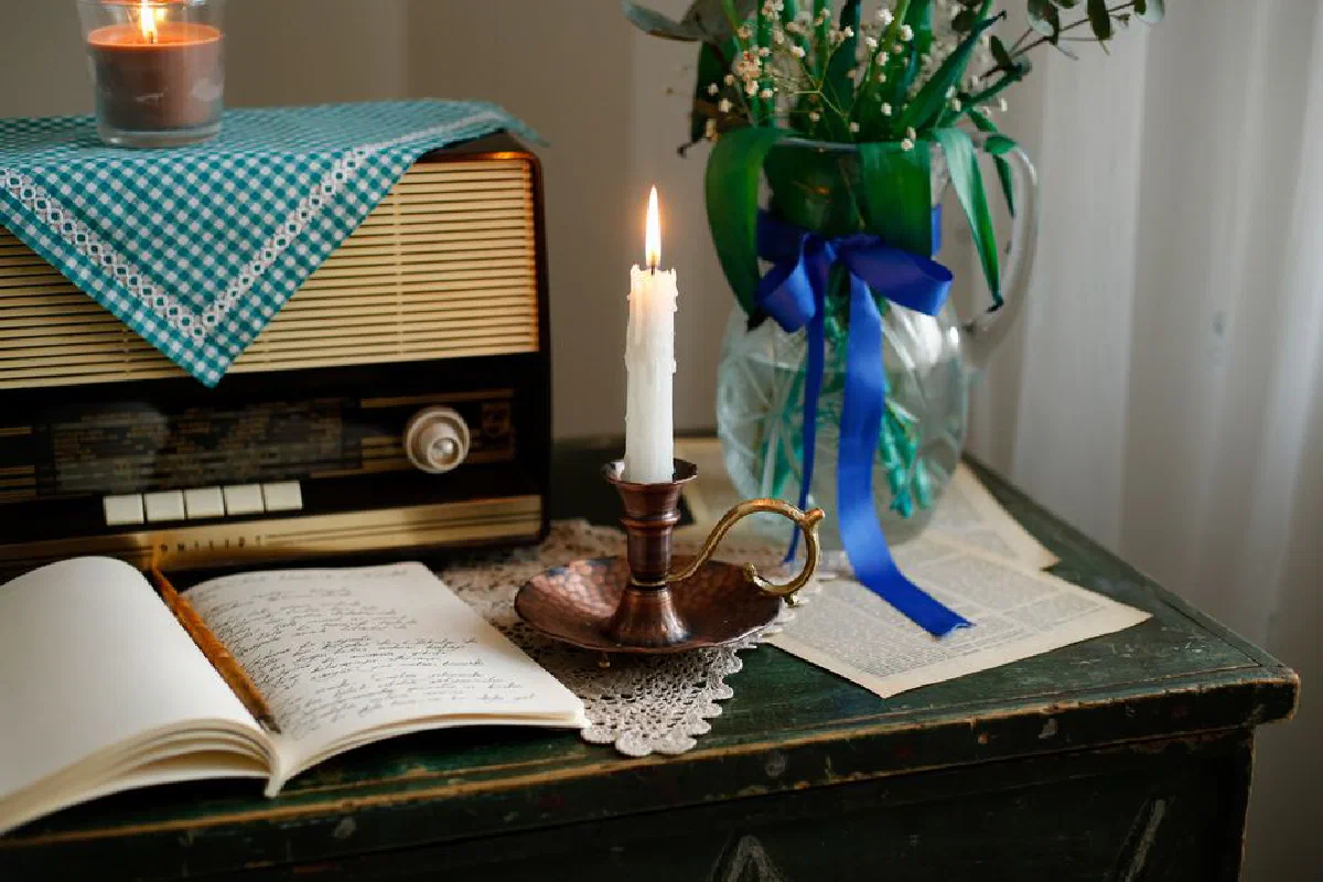 Cozy vintage setup with candlelight, retro radio, and open journal on wooden desk.