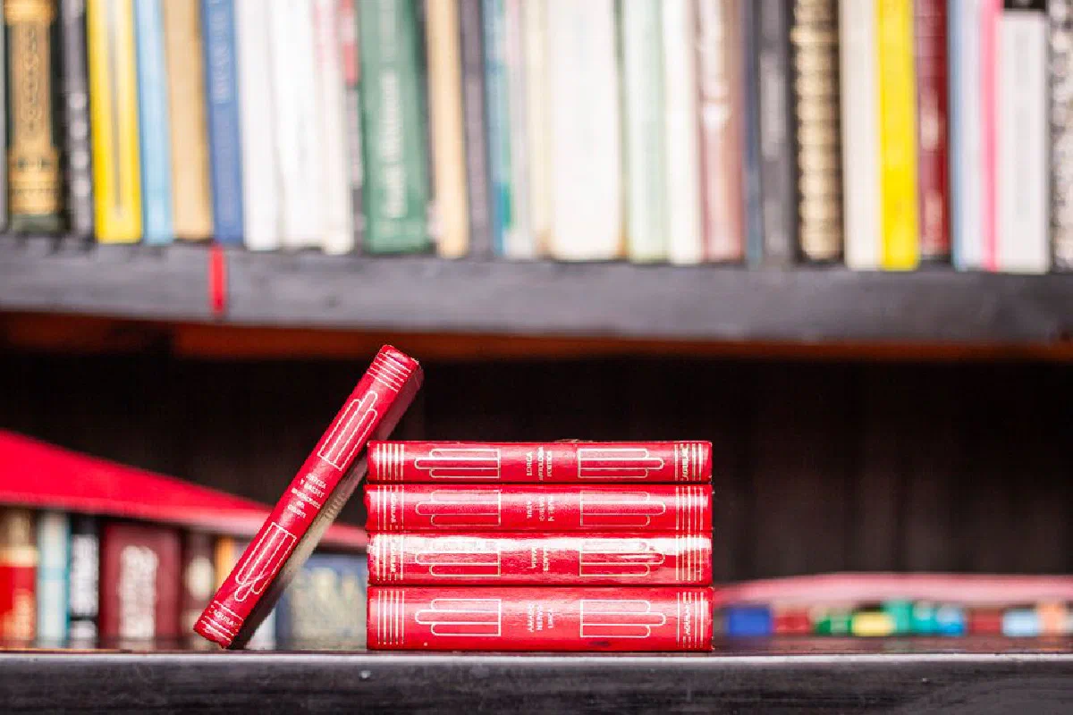 Stack of red books with a bookshelf background, ideal for library themes.