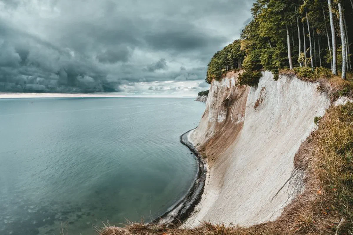 A stunning view of a dramatic coastal cliff overlooking the calm sea and cloudy sky.