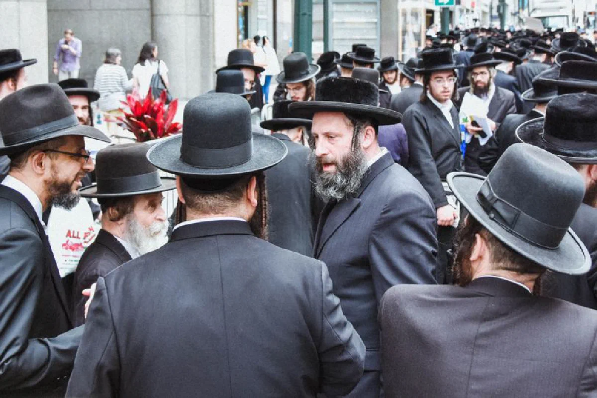 Group of Orthodox Jewish men gathered on a busy street in New York City.