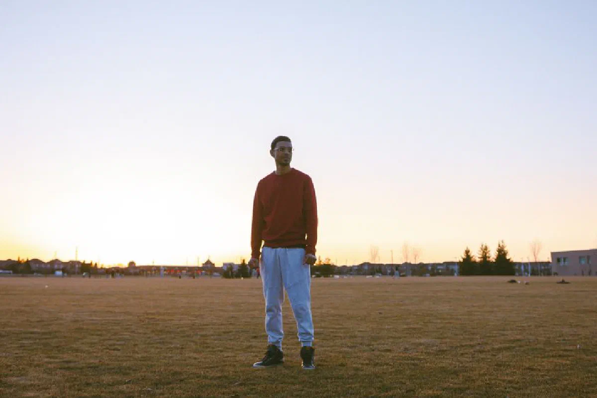 A solitary man stands in an open field during sunrise, wearing a red sweater.