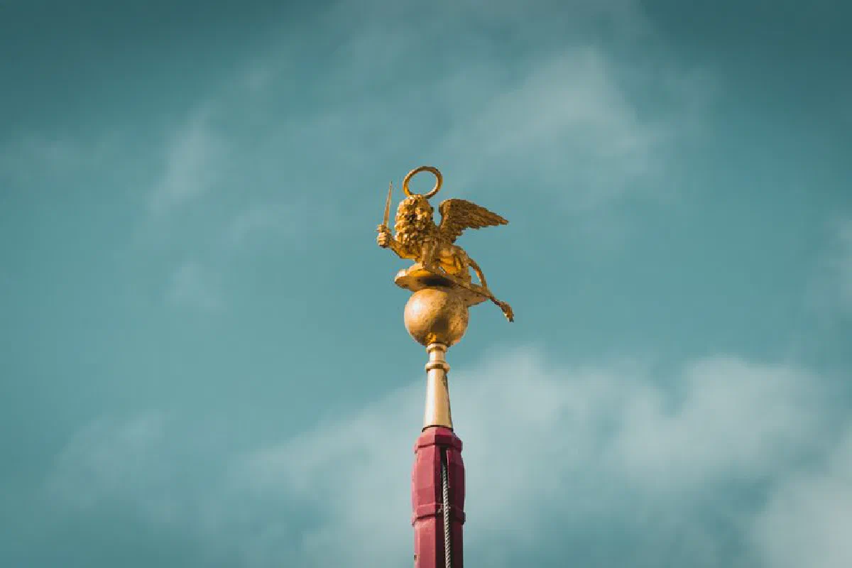 A golden winged lion statue atop a pole set against a cloudy sky in Venice, Italy.