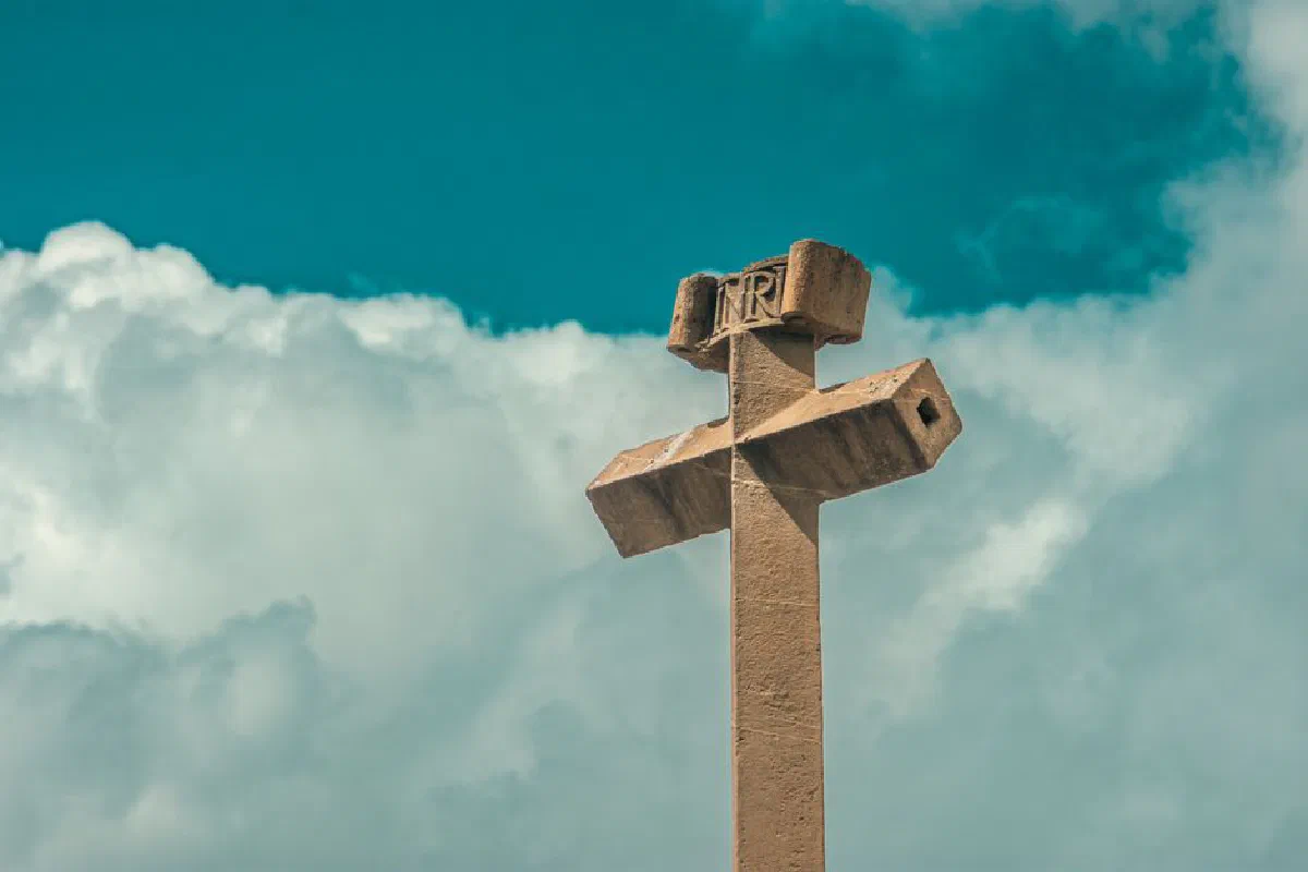 A stone cross with Christian symbols stands against a blue sky with clouds in Sucre, Bolivia.