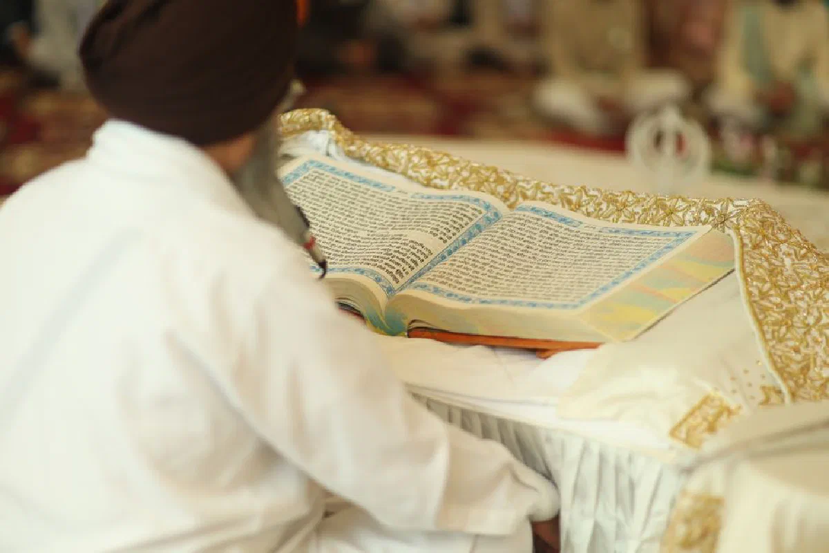 A Sikh devotee reading the Guru Granth Sahib inside a gurdwara, focusing on spiritual text.