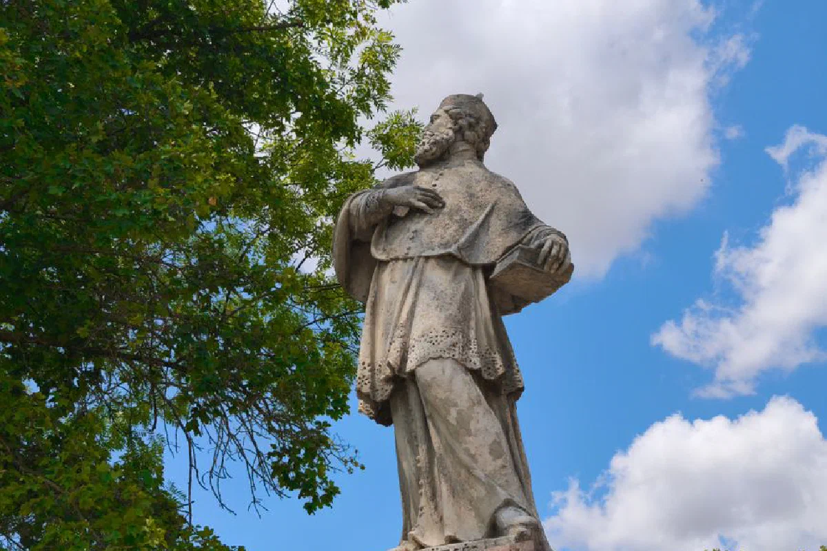 A historic stone statue against a blue sky with trees.