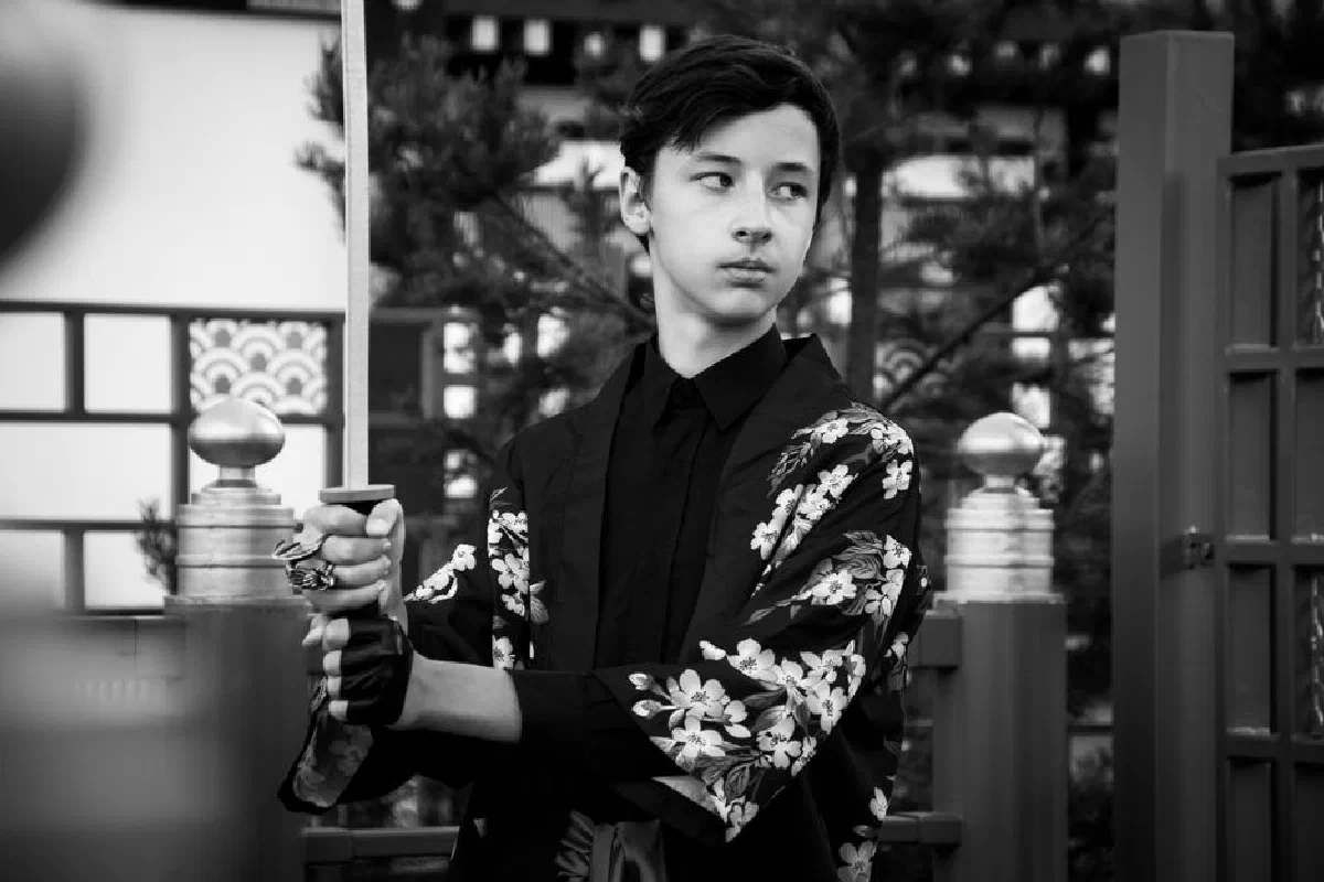 Black and white portrait of a teenage boy in kimono holding katana, embodying Japanese culture.