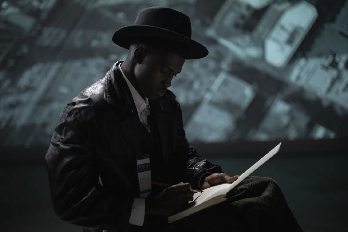 A man in a fedora and leather jacket writes indoors, symbolizing mystery and journalism.