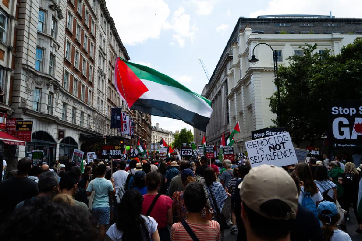 Crowd in London protests for Palestinian rights, waving flags and holding signs.