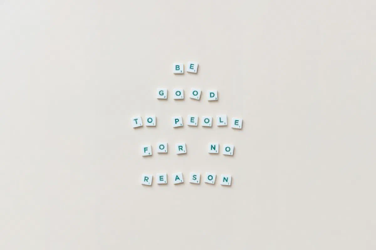 Scrabble tiles spell 'Be good to people for no reason' on a white background.