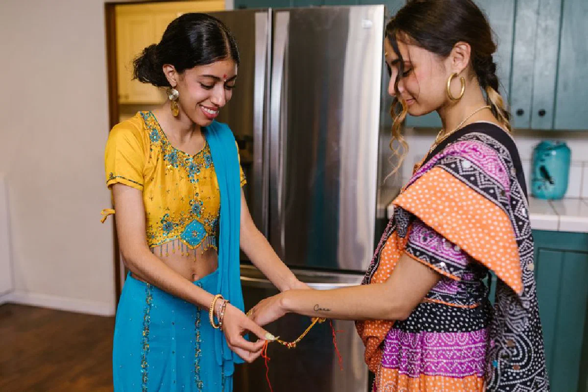 Two women in traditional clothing celebrate with a friendship ceremony, exchanging smiles and gifts indoors.