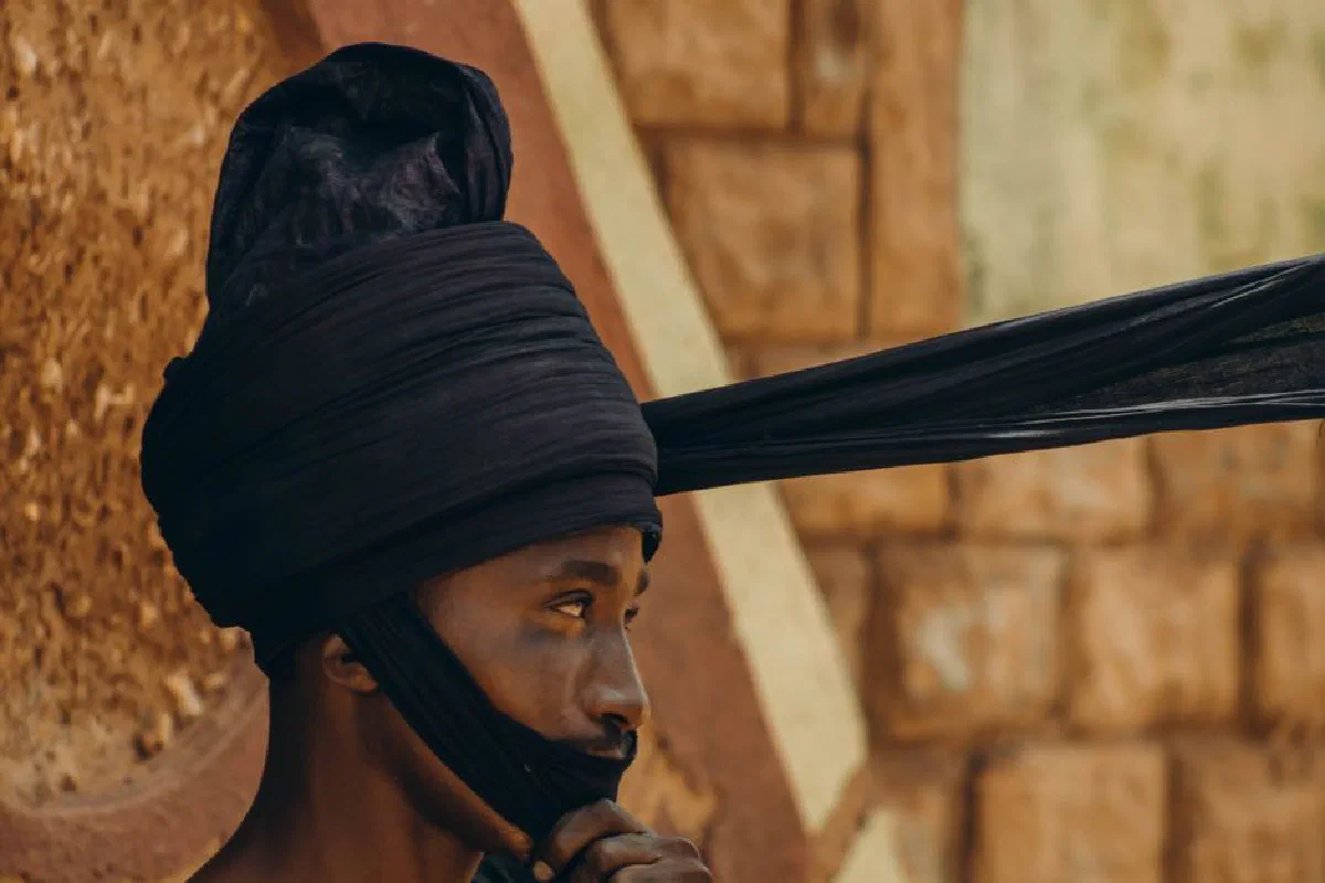 Close-up portrait of a man wearing a traditional Tuareg turban against a textured wall outdoors.