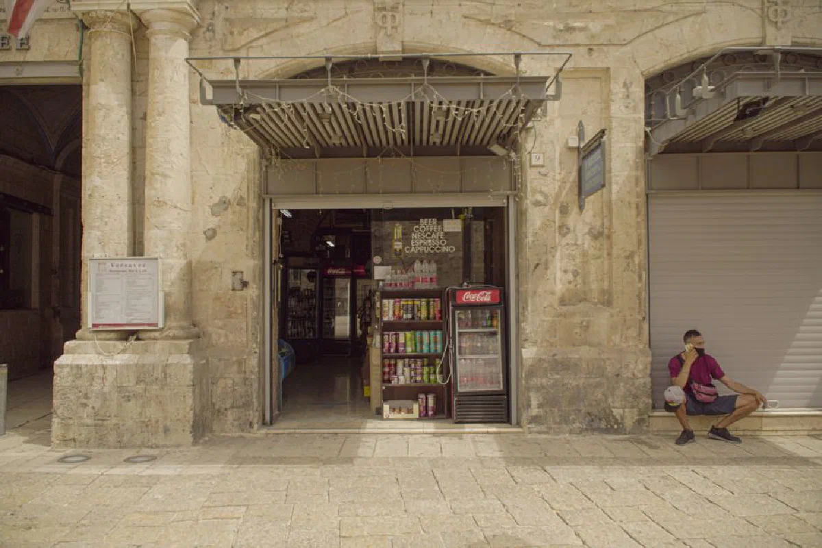 Man sitting near a shop entrance in Jerusalem's old city, showcasing historic architecture.